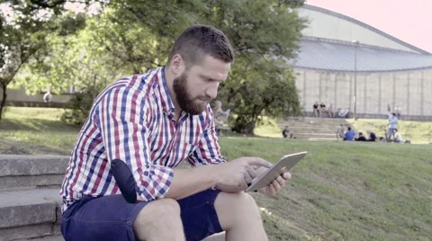 Young man writing message on tablet, sitting on stairs. Slider shot. Vídeo Stock 67248098