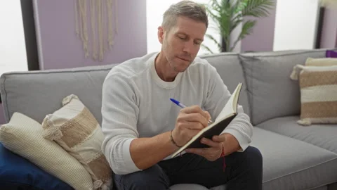 Young man writing in notebook, sitting on sofa in cozy living room, relaxed.. Stock Footage 304617520