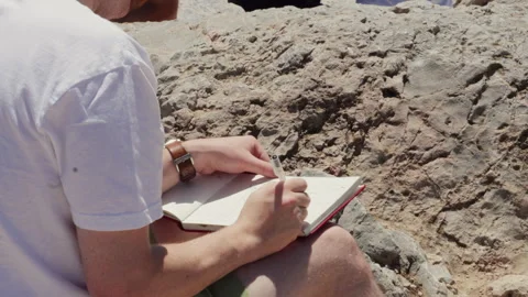 Young Man Writing in Notebook While Sitting on Rocks in Athens Stock Footage 340159160