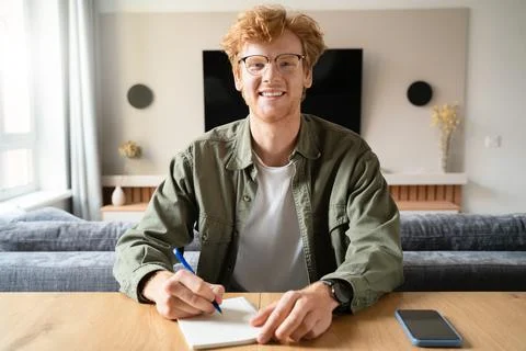 Young man writing notes looking at camera holding videoconference webcam view Stock Photos
