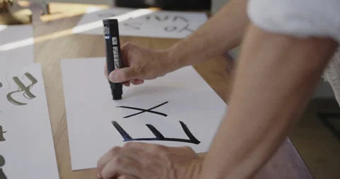 Young man writing the word “Existo” in Spanish on a desk table on a white Stock Footage 292860527