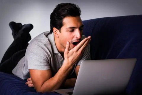 Young man yawning at computer on couch Stock Photos