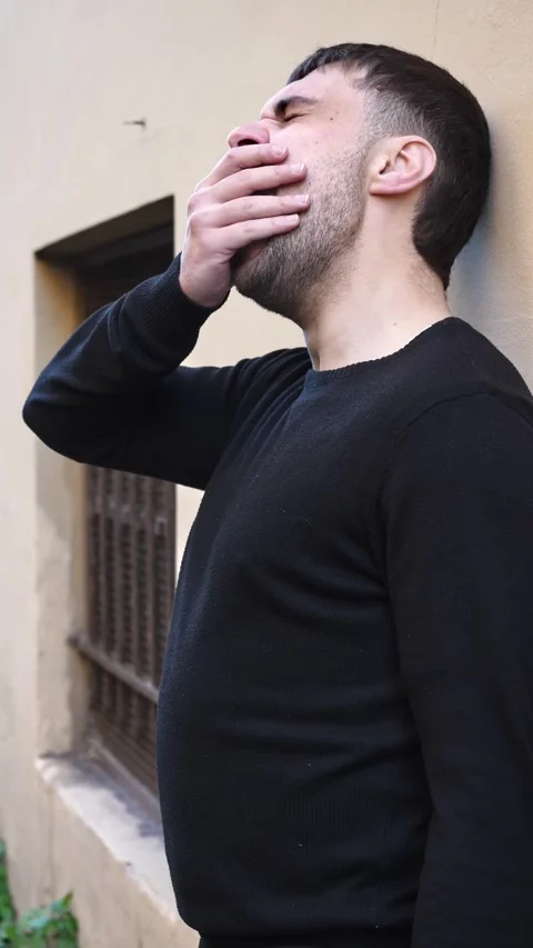 Young man yawns while leaning against a wall showing boredom and fatigue Video stock 328644567