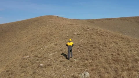 Young man in yellow hat running upside the hill. Aerial view from behind Vídeo Stock 259842205