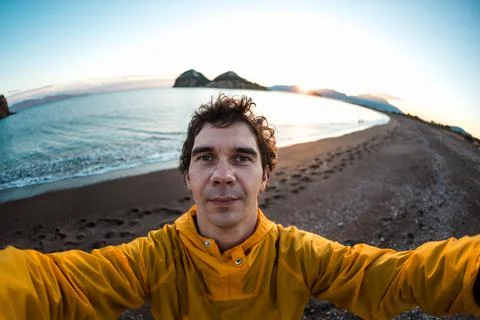 Young man in a yellow jacket makes a selfie on the seashore at sunset. travel Stock Photos