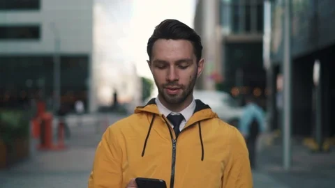 Young man in yellow jacket walking in summer street and net surfing on phone Stock Footage 95591516