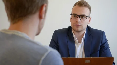 Young manager clerk with client sits at desk table. Conversation of two young Stock Footage 104598792