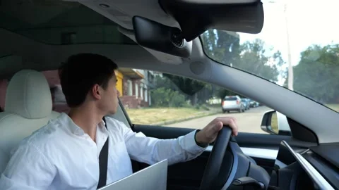 Young manager driving modern electric car reversing out of his home driveway. Ma Stock Footage 344767916