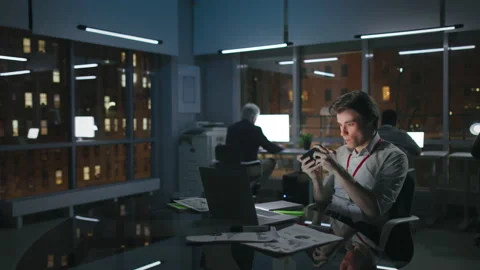 Young manager play video game on smartphone working late in loft office in Stock Footage 174609491