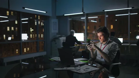 Young manager play video game on smartphone working late in loft office in Stock Footage 243631407