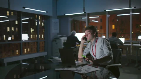 Young manager talk on phone working late in loft office with night city view Video stock 174615378