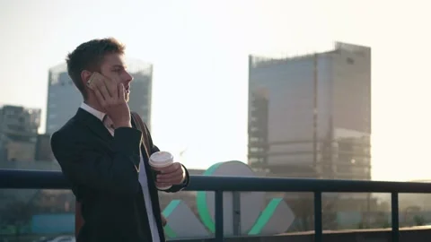 Young manager talking on the phone in the city and drinking coffee. The camera Stock Footage 165383982