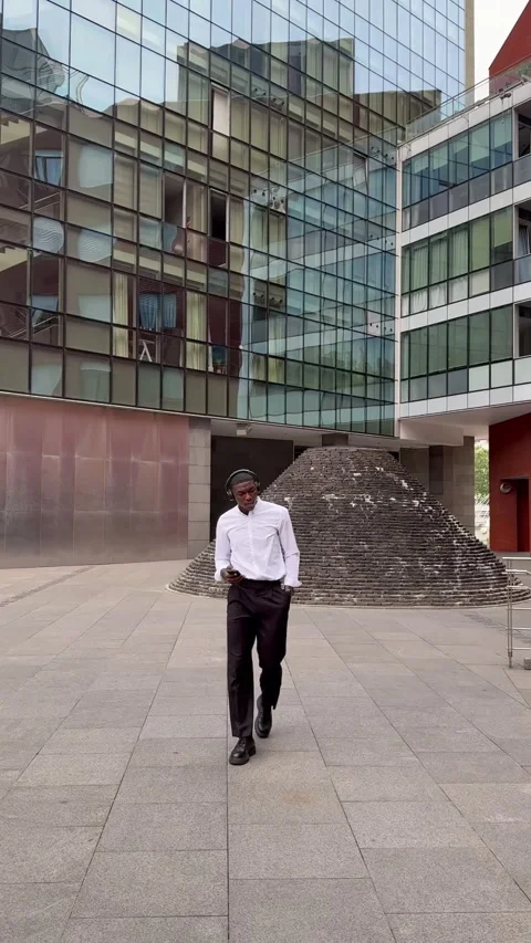 Young manager walking and listening to music in urban setting Stock Footage 310750341