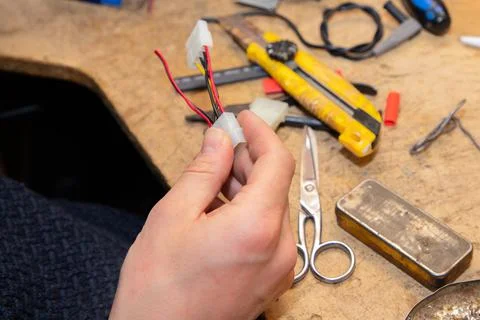 Young man's hands hold multicolored wires over desk with tools Stock Photos