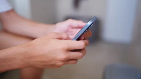 Young man's hands holding and using a modern smartphone, scrolling through .. 動画素材 340387527