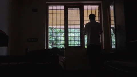 A young man's silhouette in front of the window loneliness alone black and white Stock Footage 127687435