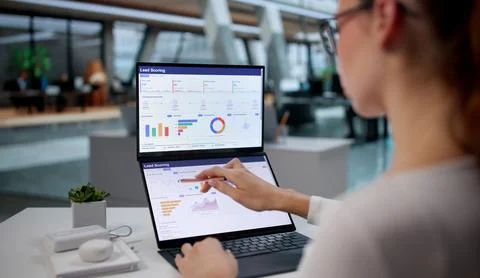 Young Marketing Manager Studies Data On Dual Touchscreen Laptop With Focus. Stock Photos