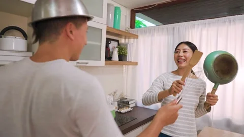 Young married couple doing a pretending casual fight with utensils and pans in Stock Footage