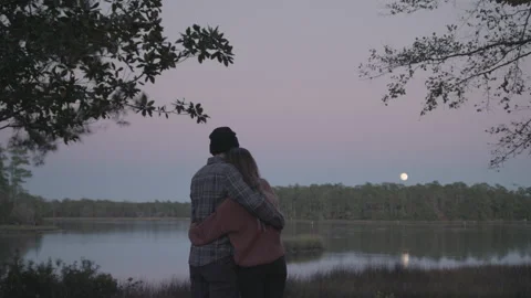 Young Married Couple Embrace While Watching the Moon Rise over the Trees Stock Footage 208780325