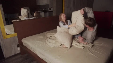 A young married couple having fun in a big bed in a hotel, they play and fight Stock Footage 145074661