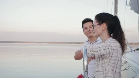 Young married couple in red pants sits on the side of a white sailing yacht Vidéo 119004117