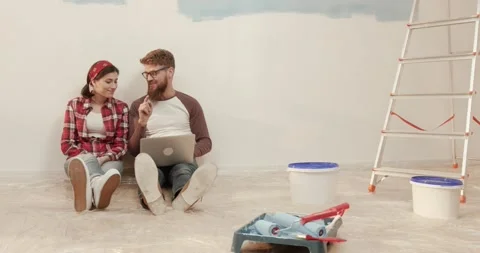 Young married couple sitting on floor near ladder and buckets of paint and Stock Footage 147059007
