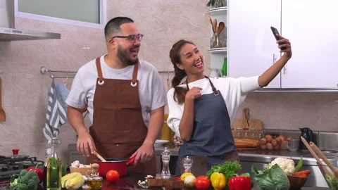 Young married couple using smartphone taking selfie while cooking in the kitchen Stock Footage 134414324