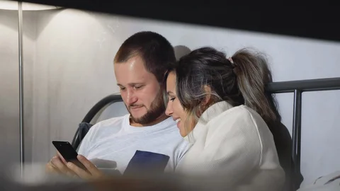 Young married couple using their mobile phone while lying in bed and smiling Stock Footage 128519716