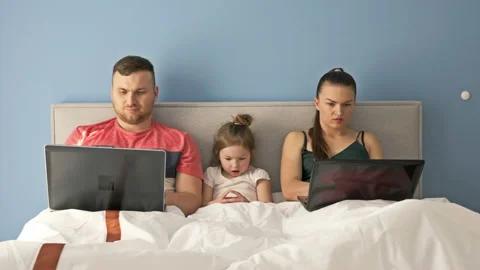 Young married couple working with laptops while lying in bed. Little girl is Stock Footage 129690454