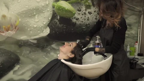 Young master in black apron washes client hair gently 스톡 동영상 107770681
