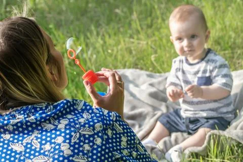 Young mather inflating soap bubbles for Surprised baby boy sitting on grass Stock Photos