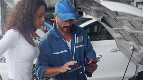 Young mechanic holding tablet talking and explaining with customer about prob Stock Footage 154033099