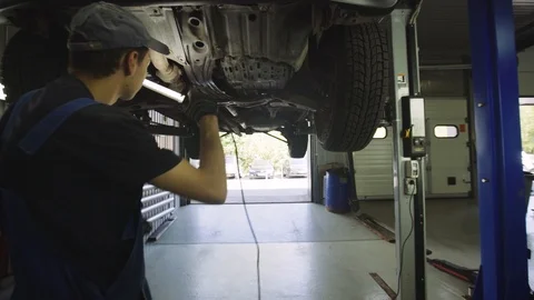 Young mechanic with light in hands looking at steering chassis under a car Stock Footage 95111487