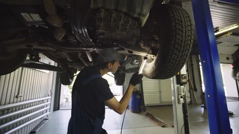 Young mechanic with light in hands looking at steering chassis under a car Stock Footage 95111579