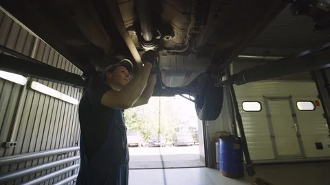 Young mechanic with light in hands looking at steering chassis under a car Stock Footage 95111740