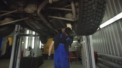 Young mechanic with light in hands looking at steering chassis under a car Stock Footage 95111951
