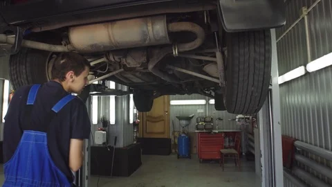 Young mechanic with light in hands looking at steering chassis under a car Stock Footage 95112022