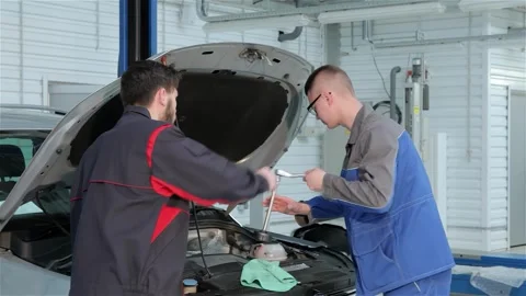 Young mechanic troubleshooting car issues with a focused partner at the service Stock Footage 311232689