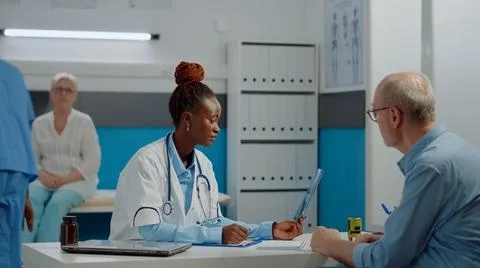 Young medic explaining x ray result to old man at desk Stockfoto's