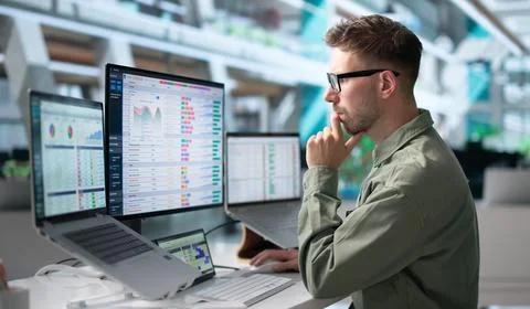 Young Medical Coder Reviews Billing Codes On Laptop In Busy Office. Stock Photos