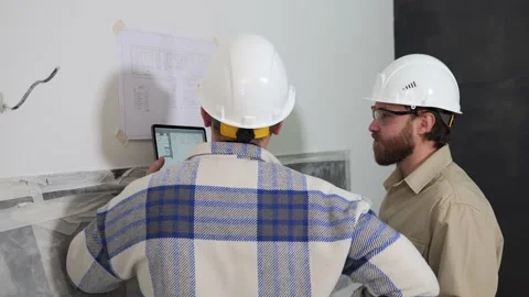 Young men, an architect and a foreman analyze a plan drawing hanging on the wall Stock Footage 234411759