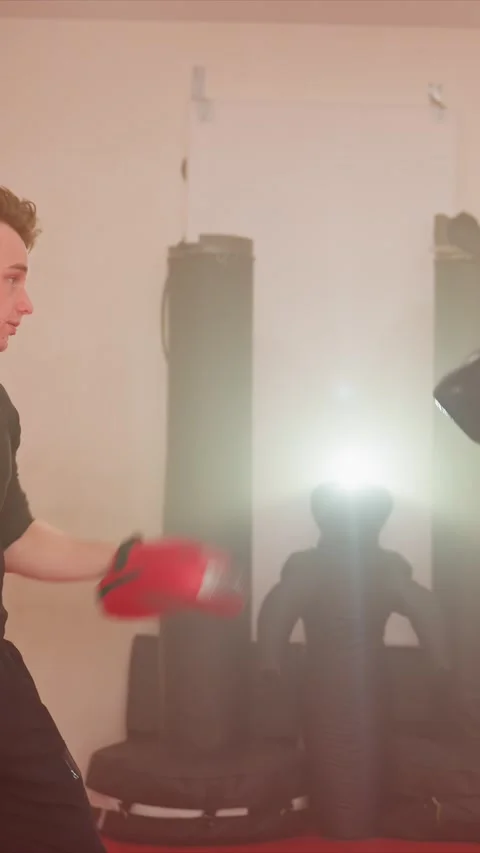 Young men in black boxing gloves practice punches towards red focus mitts Stock Footage 343093336