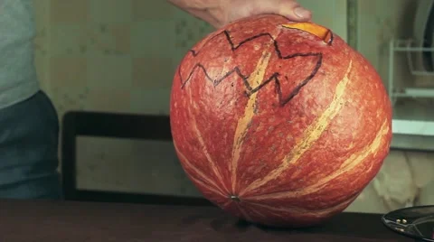 Young men carves jack o lantern out of pumpkin on a kitchen table using knife Video stock 68177828