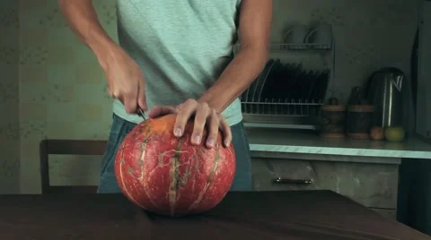 Young men carves jack o lantern out of pumpkin on a kitchen table using knife Stock Footage 68181059