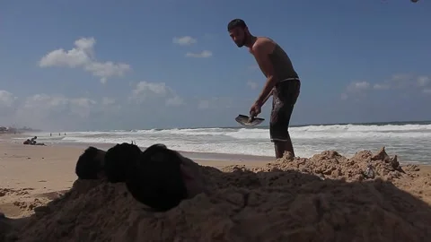 Young men have fun hiding their bodies in the sand Stock Footage 148625536