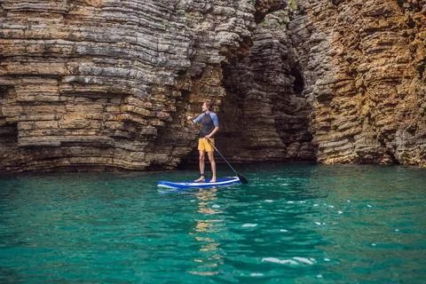 Young men Having Fun Stand Up Paddling in blue water seaamong the rocks in Stock Photos