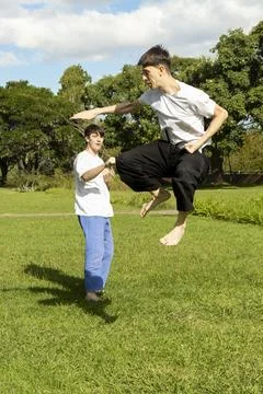 Young men practicing dynamic Taekwondo jumps in a park Stock Photos