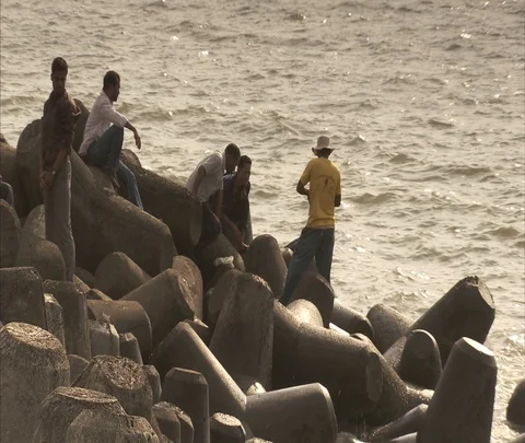 Young men sitting on wavebreakers at Nariman Point. Stock Footage 86741877