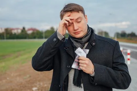 Young men is suffering from a cold while holding a handkerchief. Outdoor back Stock Photos