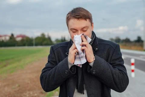Young men is suffering from a cold while holding a handkerchief. Outdoor back Stock Photos